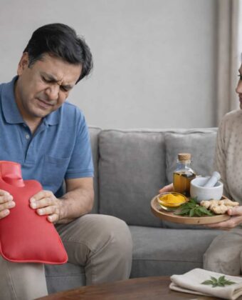 Middle-aged man experiencing joint pain holding a hot water bag while a woman offers natural remedies like turmeric and ginger at home.